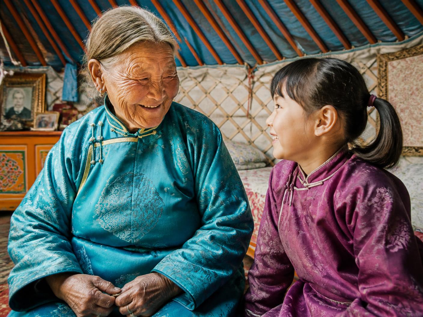 A Mongolian grandmother laughing with her granddaughter inside a ger